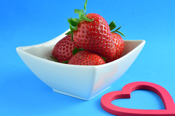 Red strawberries in a white porcelain bowl.
Blue background with copy space.