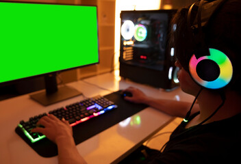 Playing on computer, teenage gamer boy playing on computer in his room at night. Room and computer has warm neon lights. 