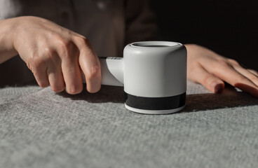 Woman removing lint from fabric with shaver. Handheld electric defuzzer. Hands closeup. High quality photo