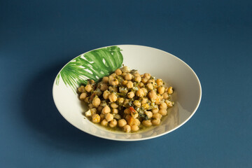 White plate decorated with green leaves with a serving of chickpeas with spinach. Traditional recipes.