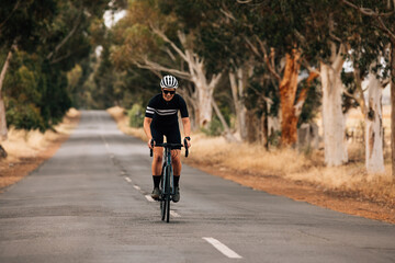 Woman standing out of the saddle on road bike while riding. Pro cyclist exercising on empty road.