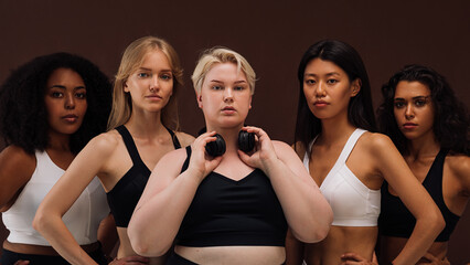 Group portrait of young confident women in sports clothes standing together on brown background