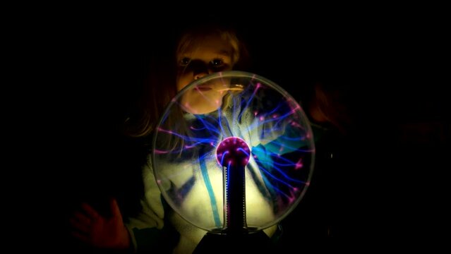 Pretty little girl moves her fingers across the surface of the plasma Tesla ball
