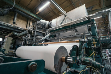 Production machine with rolls of new paper in waste paper recycling factory.