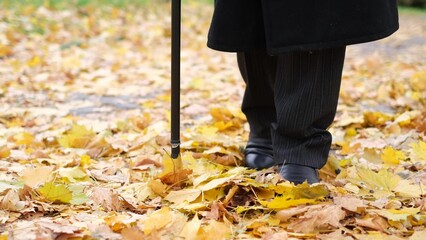 An elderly man with visual impairments tries to walk through the city's autumn park.