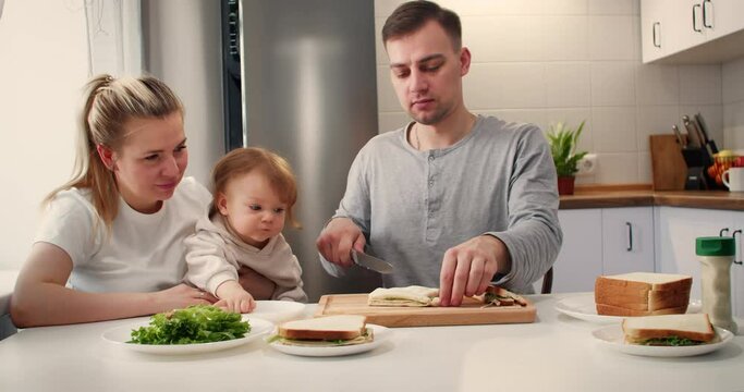Father cooking sandwiches for mother and little doughter for breakfast at home. Happy smiling family having a breakfast in a kitchen