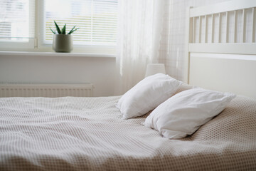 The interior of the room in white tones with a bed, bedside table, table lamp and a flower on the windowsill