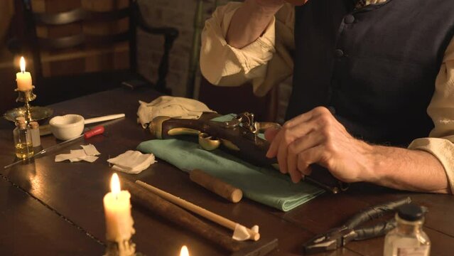 A man from the 1700s takes a sip of coffee before he starts the process of cleaning his flintlock pistol.