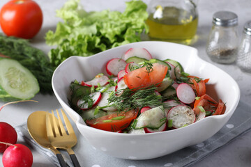 Salad with cucumbers, tomatoes and radishes dressed with olive oil in white salad bowl on a gray background