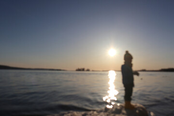 blurry photo of a child's silhouette against the background of a river at sunset  
