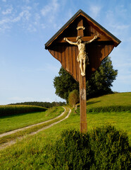 a footpath in the fields and a wooden cross with Jesus Christ in the Bavarian village Konradshofen (Germany)	