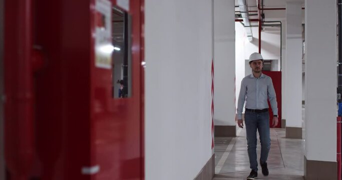 Engineer in helmet walks along long corridor at underground parking lot. Professional worker prepares for implementation of new project