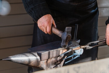 Selective focus close-up of a blacksmith's hand with a hammer on a metal anvil and a metal part, a beam of sunlight illuminates the metal. Illustration of hard manual labor and craftsmanship