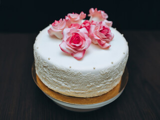 Obraz na płótnie Canvas A single tier white wedding cake with pink rose flowers from a pastry glaze. Holiday sweets.