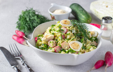 Salad with Chinese cabbage, cucumber, radish, chives and quail eggs in white plate on a gray background
