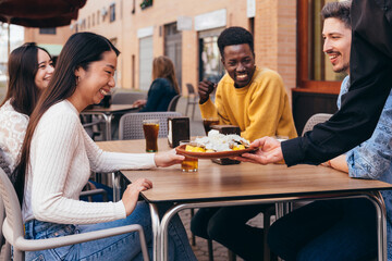 interracial gathering of friends happy because a waiter is serving them food
