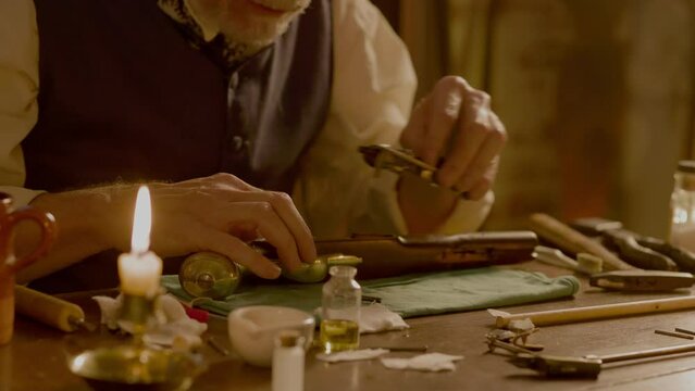 A man in the 1700s returning the lock mechanism to the flintlock pistol he has been cleaning.