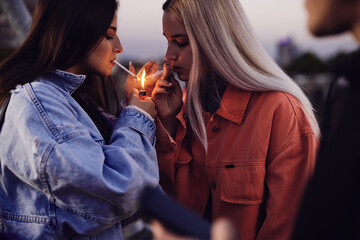 Two rebellious teenage girls lightning cigarettes and smoke. Teenagers smoking cigarettes