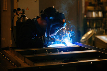 Fototapeta na wymiar Factory worker in protective mask welding iron parts