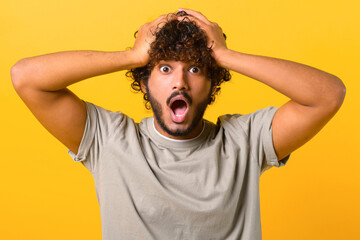 Excited shocked Indian man holding hands on head and screaming looking at camera with big eyes and...