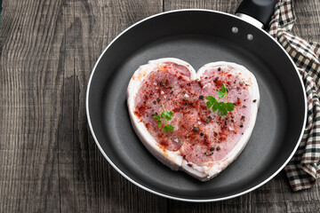 Heart shaped raw fresh pork slices with parsley and herbs on frying pan on wooden table