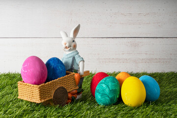Easter bunny on his cart carries colorful eggs on a white background