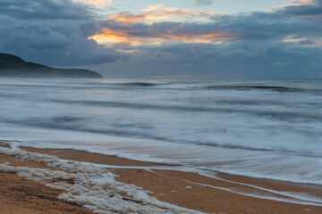 Sunrise seascape with sea foam and rain clouds