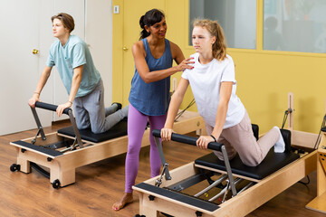 Pilates instructor helps and monitors the difficulty of Pilates exercise for an teenagers