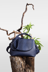 Blue leather handbag on wooden snag. Creative fashion minimal background.