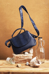 Still life with blue women's handbag and objects made of natural materials and glass. Eco leather handbag and objects on wooden table.