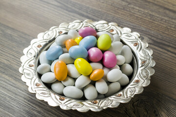 Traditional, white and pastel tones colored, chocolate covered almond candies in silver vintage bowl, on wooden surface	