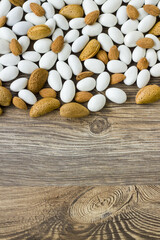 Traditional, white colored, chocolate covered almond candies with almonds nuts on wooden surface, vertical image