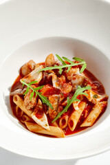 Traditional Italian dish - penne with salmon and squid with tomato sauce and olives. Penne marinara with seafood on white table. Italian seafood pasta in arrabiata sauce - healthy mediterrian lunch.