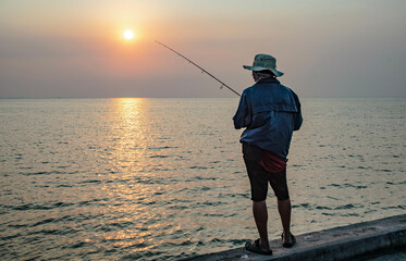 Fishermen stand fishing in the evening at a local fishing boat pier called Saphan Pla at Ban Na Kluea, Bang Lamung District, Thailand