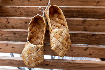 Birchen woven bast shoes hang on a log wall.