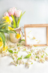 Wooden plate with a place for your texts and flowers tulips and white petals on a light wooden background.