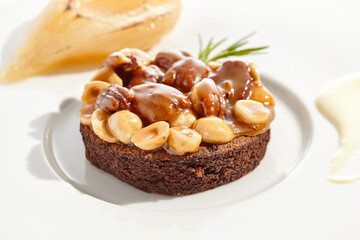 Chocolate tartlet with nuts toffee on white plate. Delicious dessert - Caramel nut tart with pear. Traditional pastry - Butterscotch tartlet with hazelnut, almond and pecan. Autumn dessert