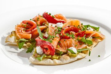 Bruschetta with salmon, avocado and paprika on white plate. Salmon bruschetta on crispy focaccia. Appetizer with guacamole, trout, cheese and paprika on toast. Fish antipasti in restaurant menu.
