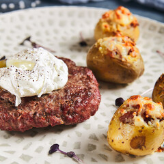 American breakfast - beefsteak with egg and roasted baby potatoes. Beef cutlet with poached egg in and potatoes in plate on stone background. Egg yolk on beef steak. Main course on meat.