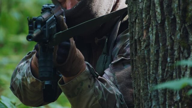 Close up military soldier man fires from a machine gun. Sitting in firing position in dense forest