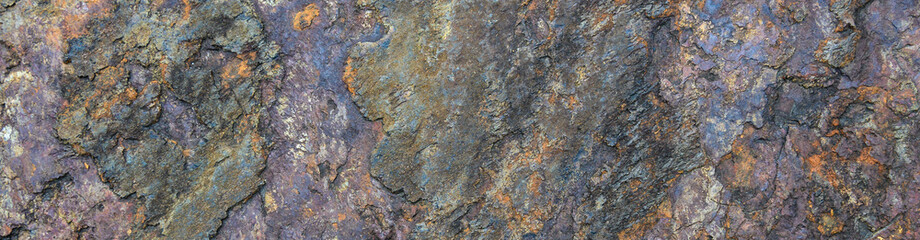 Rough cut rock in dark colors of orange, gray, purple, and blue, as a natural  background
