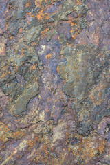 Rough cut rock in dark colors of orange, gray, purple, and blue, as a natural  background
