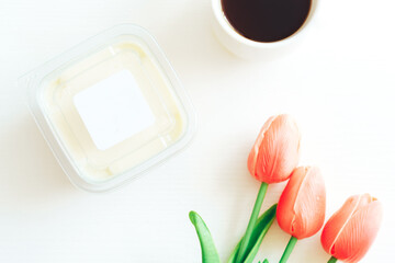White chocolate in plastic container next to coffee and tulips.