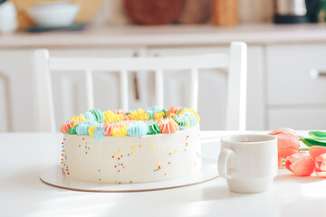 Cake decorated with multi-colored cream next to tulips and coffee.