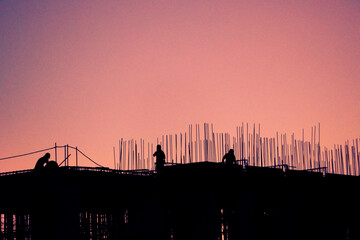 Obraz premium Silhouette of men working on terrace of building under construction, dramatic sunset in latin america.