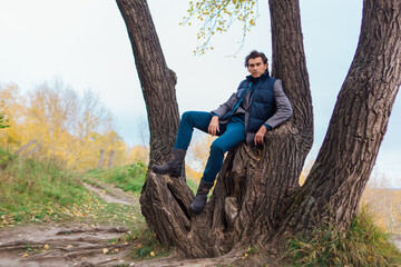 Naklejka na ściany i meble Tall handsome man climbing on the tree in autumn forest