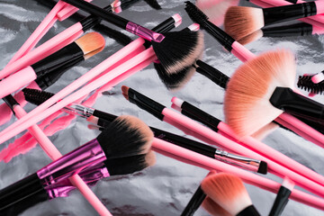 Set of pink make-up brushes. They are on a metallic background that reflects the objects. Makeup concept.
