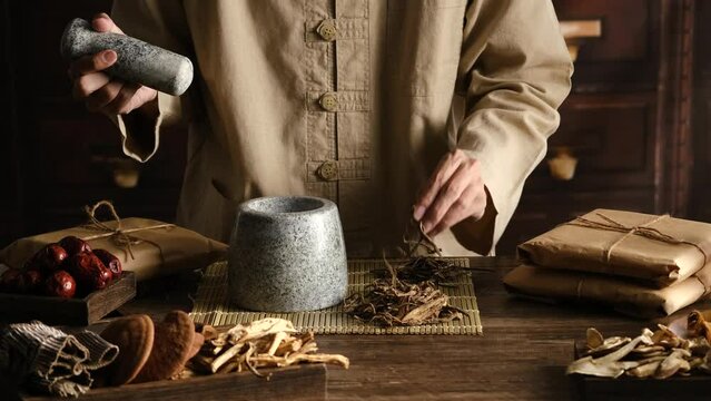 Front view of apocathery putting ingredient into mortar and pestle with chinese traditional medicine in wooden table 