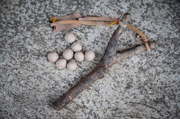 A wood slingshot with clay balls on the cement floor. A slingshot works like a small catapult, with rubber strips holding a stone or other projectile sits.