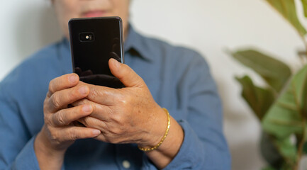 close up on mature woman hand holding smartphone to using social media or video call application or checking news on website for retirement lifestyle concept